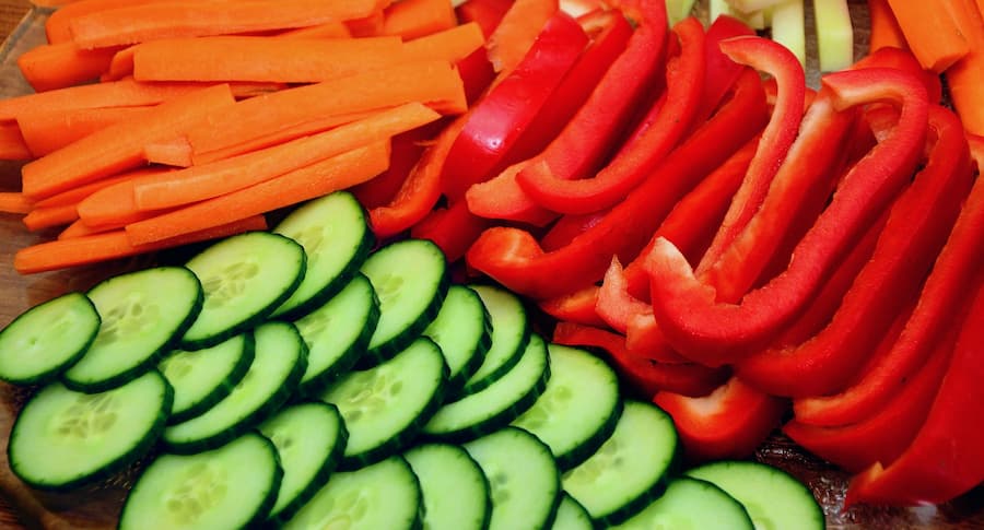 Sliced carrot sticks, red bell pepper strips and cucumber slices on a wooden board