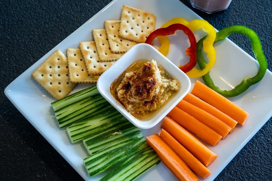 Plate of carrot and cucumber sticks with hummus, bell pepper slices and crackers