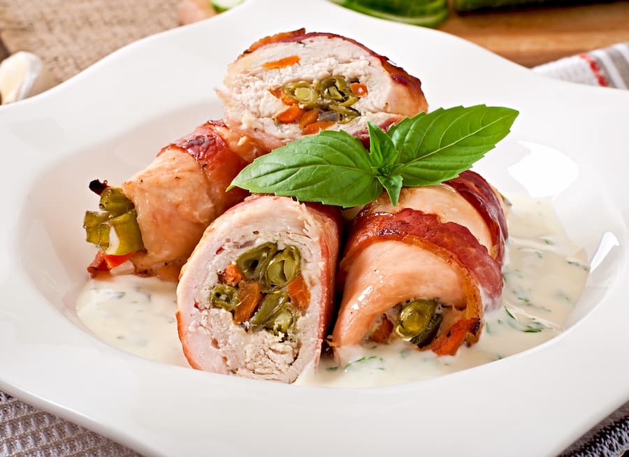 Chicken roll-ups filled with vegetables on a white plate with basil