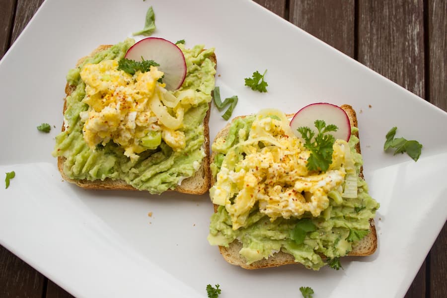 avocado toast topped with scrambled egg on a white plate