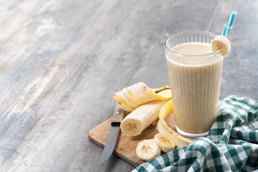 Creamy homemade banana smoothie in a glass with banana slices, a healthy school snack
