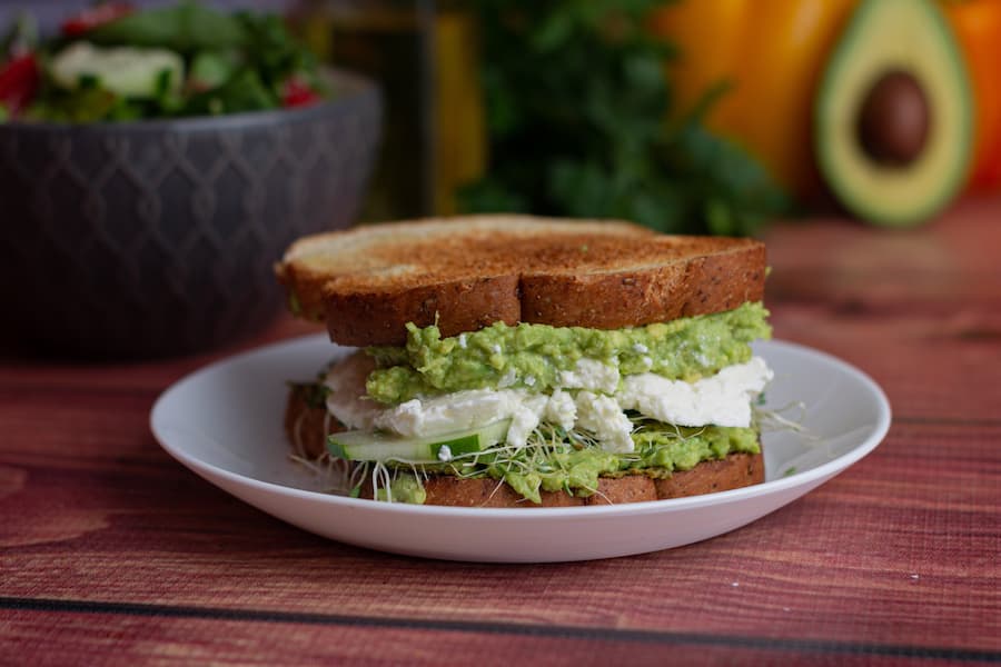 Whole-grain toast sandwich with mashed avocado filling on a white plate