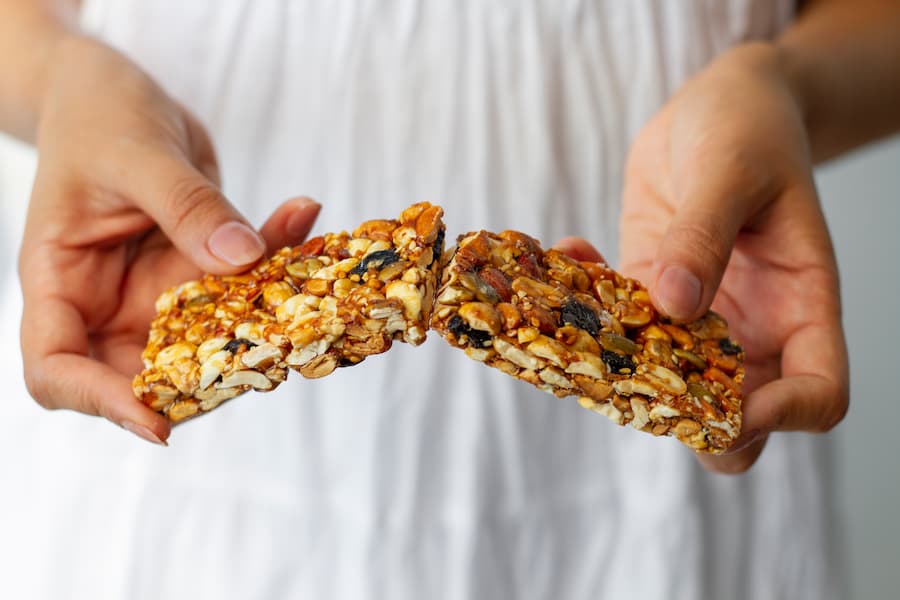 hands holding a healthy nut and seed snack bar broken in half