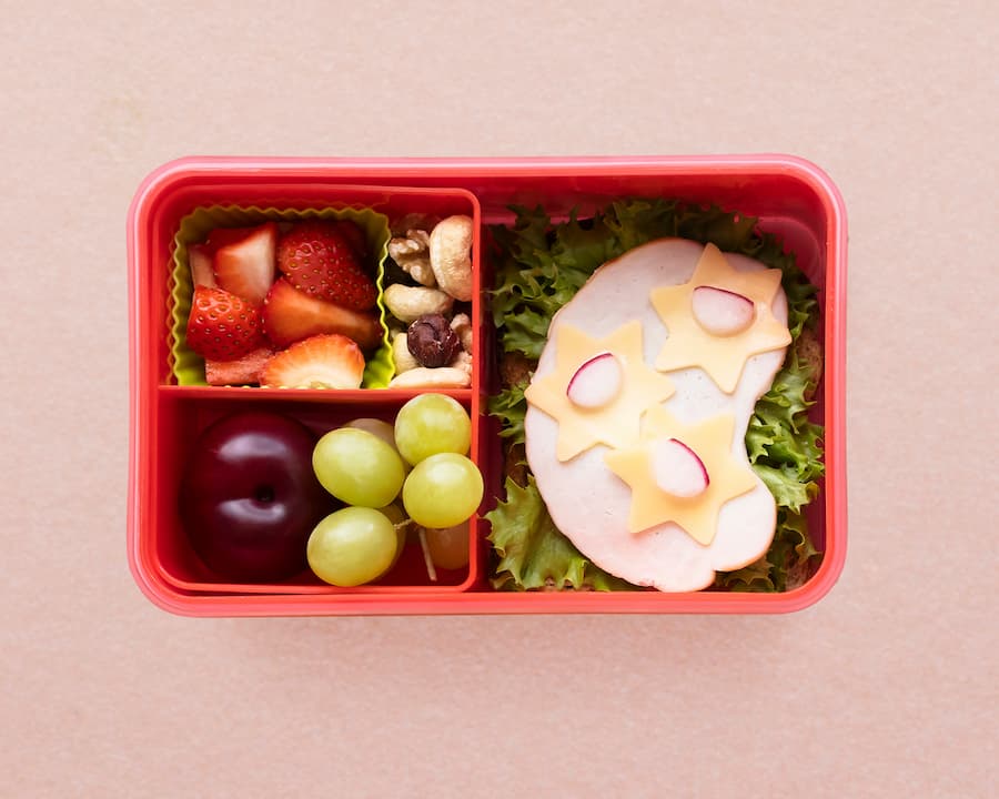 Divided kids lunch box with fresh fruit and cheese slices, a healthy school snack idea