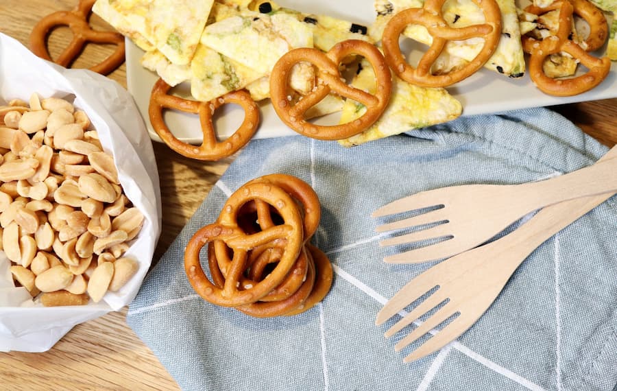 Pretzels, roasted peanuts and tortilla chips on a table with wooden forks