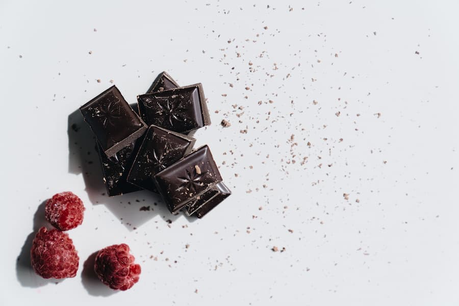 Pieces of dark chocolate squares with fresh raspberries on a white background