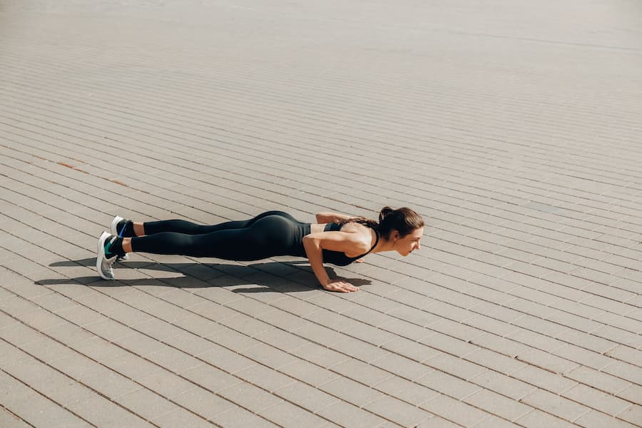 Woman doing a push-up outdoors on a paved surface as part of a home workout