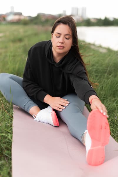 Woman doing seated leg stretch on a yoga mat outdoors