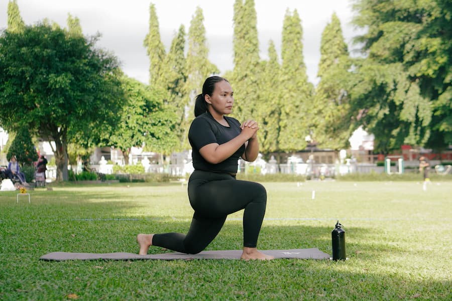 Woman doing a reverse lunge on a yoga mat in a park as part of a morning home workout