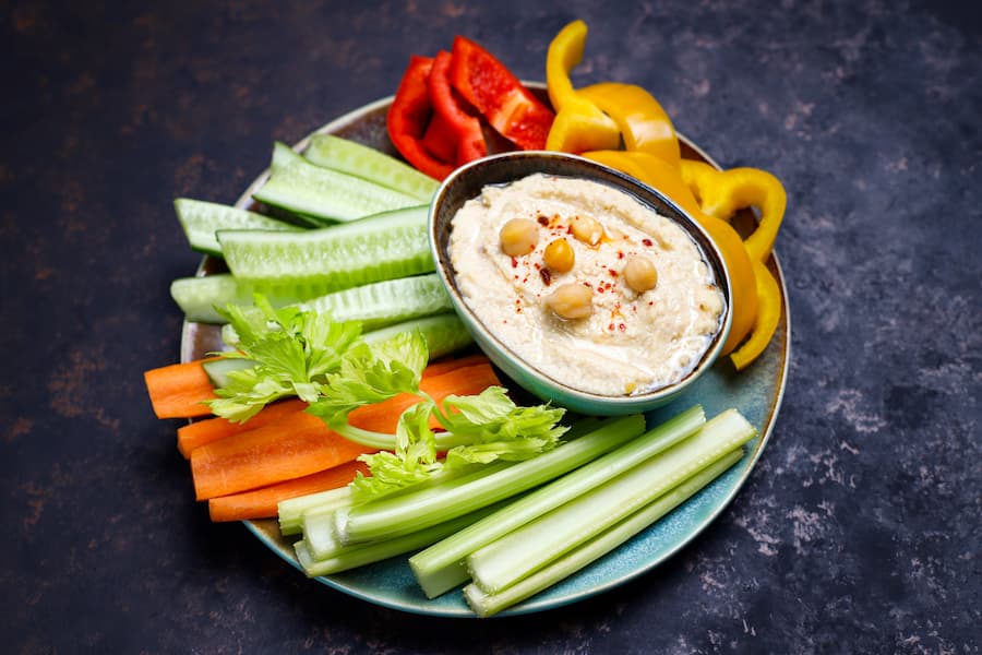 plate of carrot, cucumber, celery and bell pepper sticks with a bowl of hummus