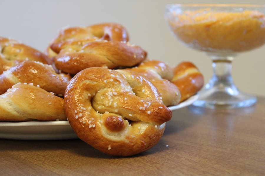 Freshly baked soft pretzels with coarse salt on a plate with a dip in a glass bowl behind