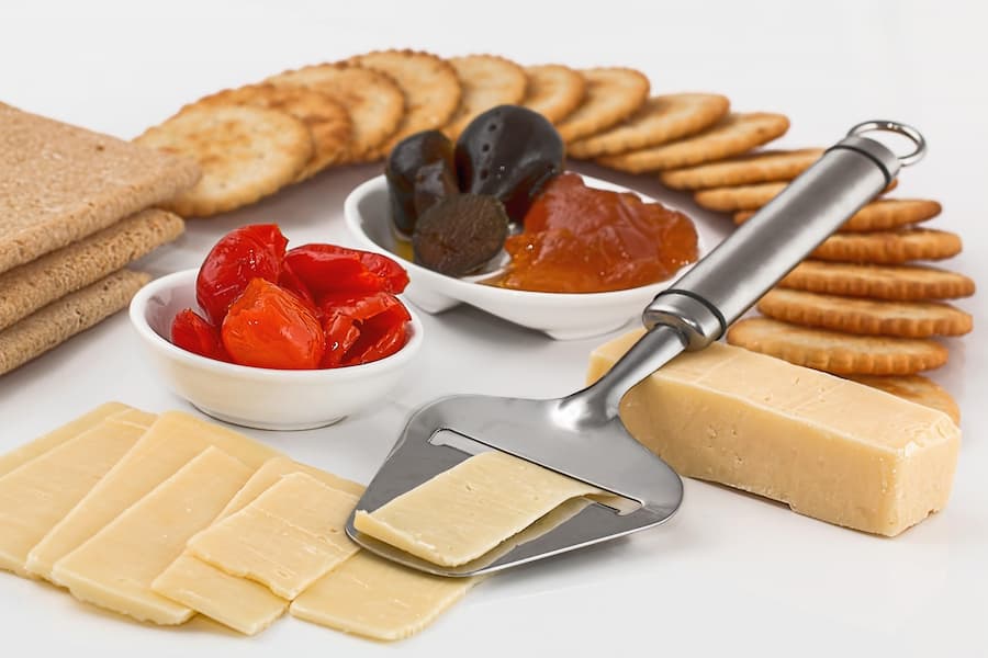 Crackers with sliced cheese and a cheese slicer on a white table