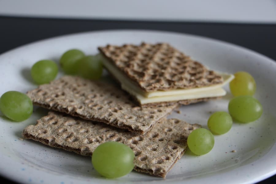 Whole-grain crackers with slices of cheese and green grapes on a white plate