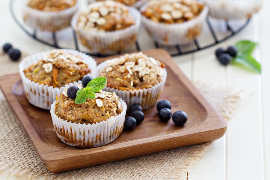 Whole-grain oat and carrot muffins with blueberries on a wooden tray, a healthy school snack