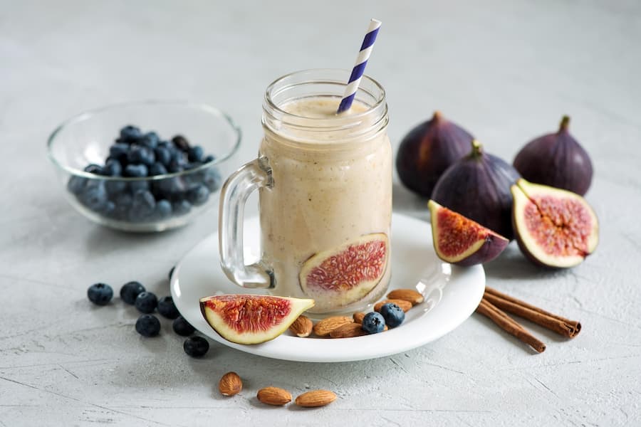 Creamy fruit smoothie in a glass jar with a striped straw, served with blueberries, figs and almonds