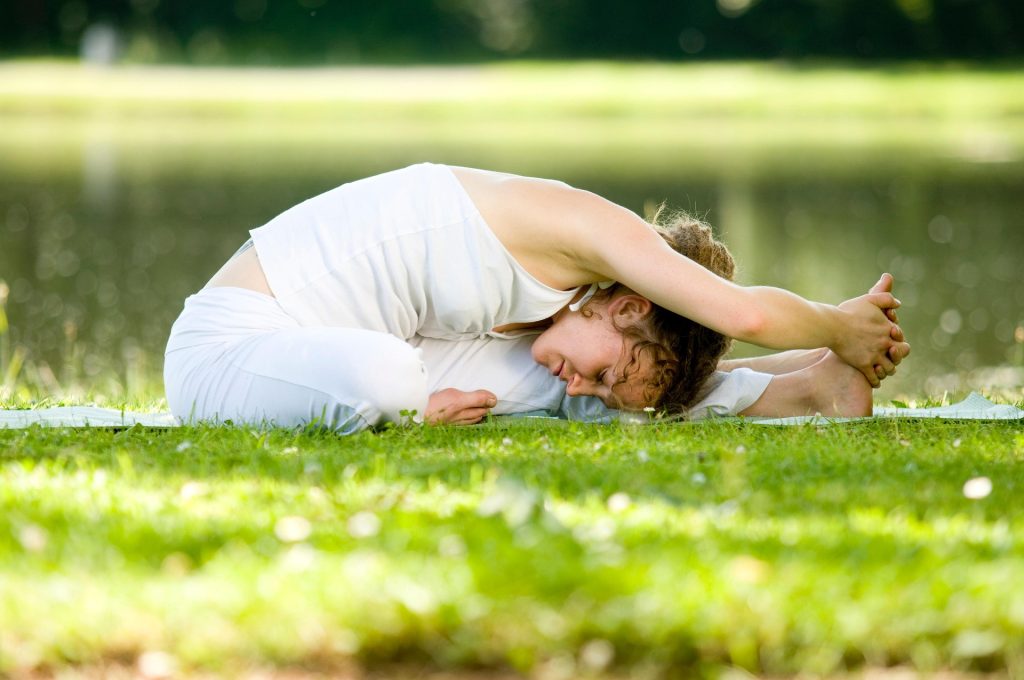 Woman doing yoga stretching exercise outdoors on grass