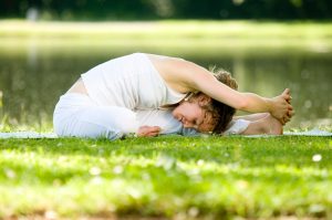Woman doing yoga stretching exercise outdoors on grass