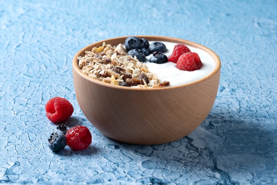 greek yogurt with granola, blueberries and raspberries in a wooden bowl