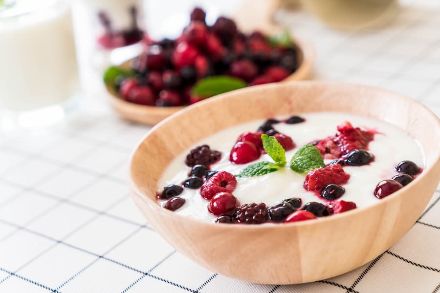 Greek yogurt topped with fresh mixed berries and mint in a wooden bowl